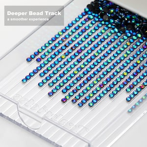 May include: A clear plastic tray with multiple parallel grooves, filled with iridescent, oval-shaped beads. The beads are arranged in rows, displaying a spectrum of colors. Text in the upper left corner reads "Deeper Bead Track, a smoother experience."