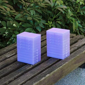 May include: Two stacks of light purple plastic storage containers, each featuring multiple small drawers with individual pull tabs. The rectangular units are arranged vertically, showcasing a translucent finish and a modular design for organising small items.