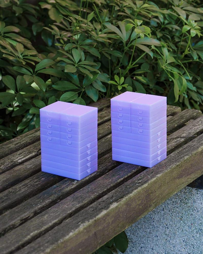 May include: Two stacks of light purple plastic storage containers, each featuring multiple small drawers with individual pull tabs. The rectangular units are arranged vertically, showcasing a translucent finish and a modular design for organising small items.