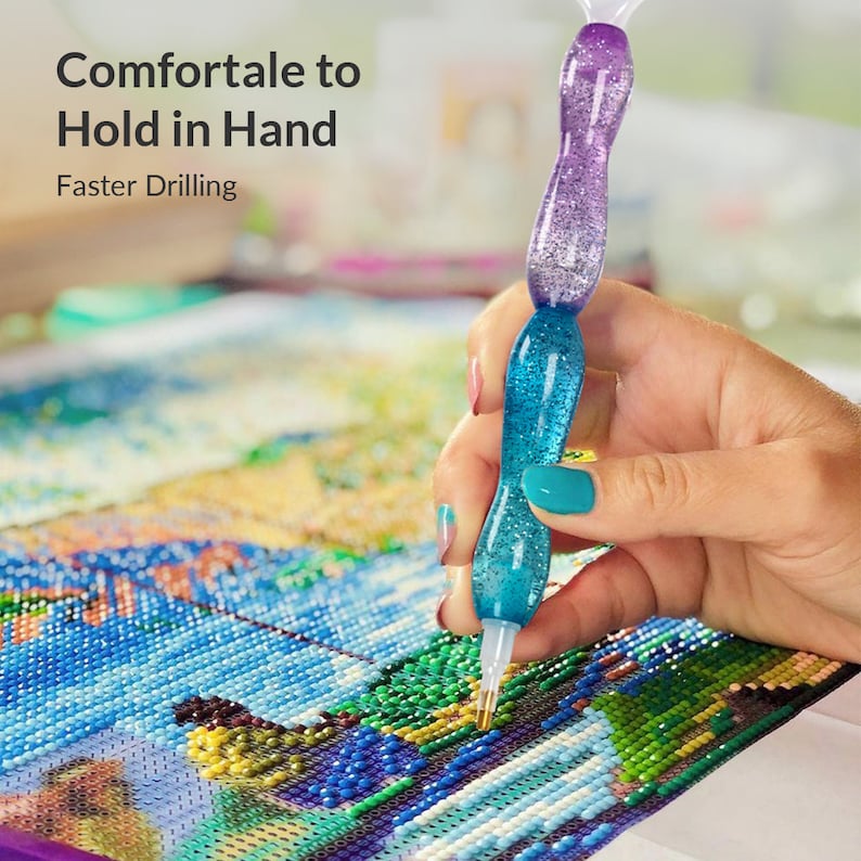 Op de afbeelding: Een close-up van een blauwe en paarse diamant schilderpen met glitter. De pen wordt gebruikt om een diamant op een diamant schilderdoek te plaatsen. De tekst "Comfortale to Hold in Hand" en "Faster Drilling" is zichtbaar bovenaan de afbeelding.