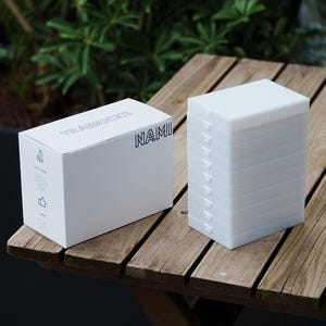 May include: A white box with the text "TRABRICKS NAMI" next to a stack of white rectangular blocks. The items are on a wooden table. The box has a small illustration and text on the side.
