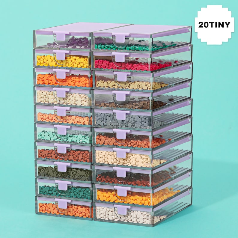 May include: A stack of clear plastic storage containers with lavender lids and latches. Each container is filled with small, colorful craft supplies. The text "20TINY" is in a white square in the upper right corner.