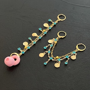 May include: Gold-toned earrings with a seashell and blue gemstone design. One earring features a pink, circular charm. The earrings have a dangling chain design with small blue gemstones and seashell charms.