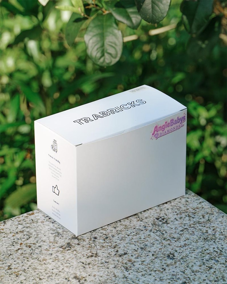 May include: A white rectangular cardboard box featuring the text TRABRICKS on the top and the logo AngieBabys Diamonds on the side. The side panel includes small black icons and text indicating travel friendly and compact features in English.