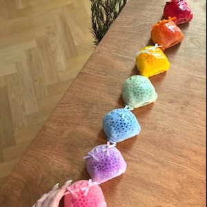 May include: A series of colourful, round, decorative objects in shades of red, orange, yellow, green, blue, purple, and pink. Each object has a dotted pattern and is tied with a small bow. The objects are arranged on a wooden surface.