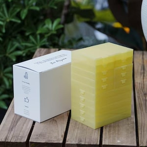 May include: A white box with the text "The Notebooks" and a yellow, stackable, plastic container with multiple compartments. The container is on a wooden surface. The box has a travel-friendly icon and a thumbs-up icon.