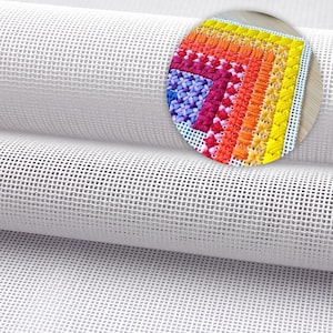 May include: A close-up of a roll of white canvas fabric with a grid pattern, suitable for needlepoint or cross-stitch. A circular inset displays a colourful cross-stitch design with various stitches in shades of blue, pink, orange, and yellow.