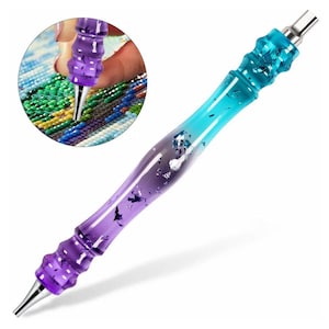 May include: A purple and blue diamond painting pen with a silver tip. The pen has a clear, glittery finish and is designed for picking up and placing diamond beads.