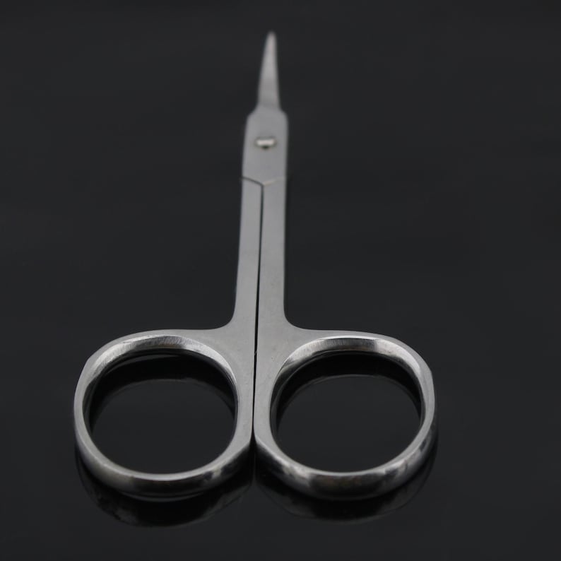 May include: A pair of small, silver-colored scissors with pointed tips. The scissors are open and the blades are visible.