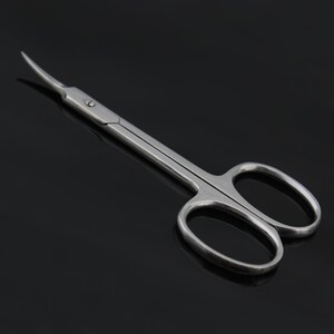 May include: A pair of silver curved cuticle scissors with a pointed tip. The scissors have two oval-shaped loops.