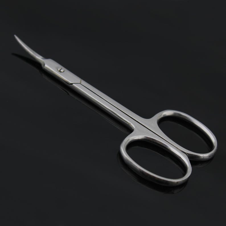 May include: A pair of silver curved cuticle scissors with a pointed tip. The scissors have two oval-shaped loops.