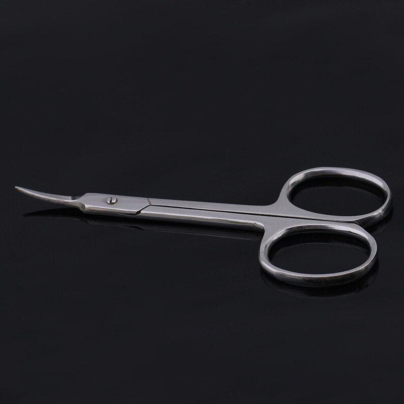 May include: A pair of silver-toned cuticle scissors with curved blades. The scissors are designed for trimming cuticles and hangnails.