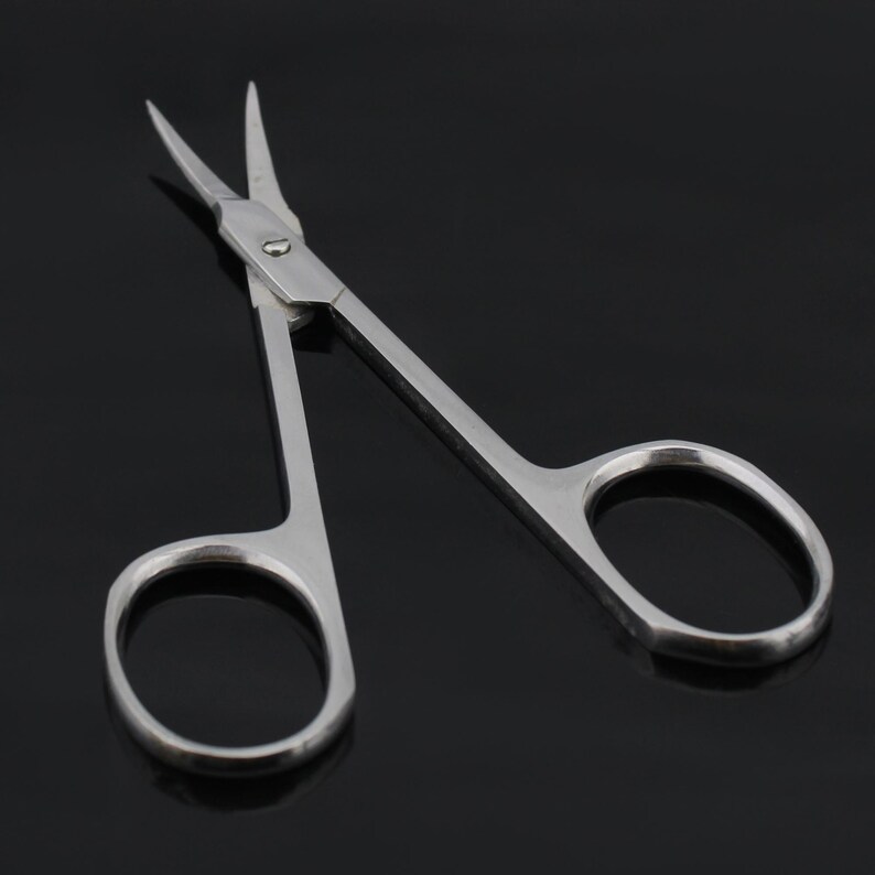 May include: A pair of silver-toned cuticle scissors with sharp pointed tips. The scissors have a small, round hole in the center of the handle.