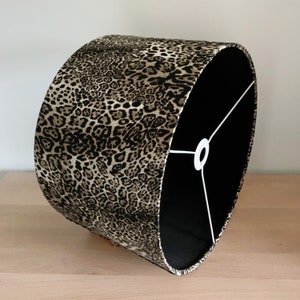 Può includere: Un paralume a stampa leopardata nero e marrone con un cavo bianco e una fodera nera.