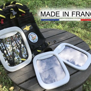 May include: Three white airplane window frames on a wooden table. The frames are made of plastic and have a clear plastic window. The frames are arranged in a semi-circle. The table is made of wood and has a dark brown finish. The table is surrounded by green grass. The text "MADE IN FRANCE" is visible in the background.