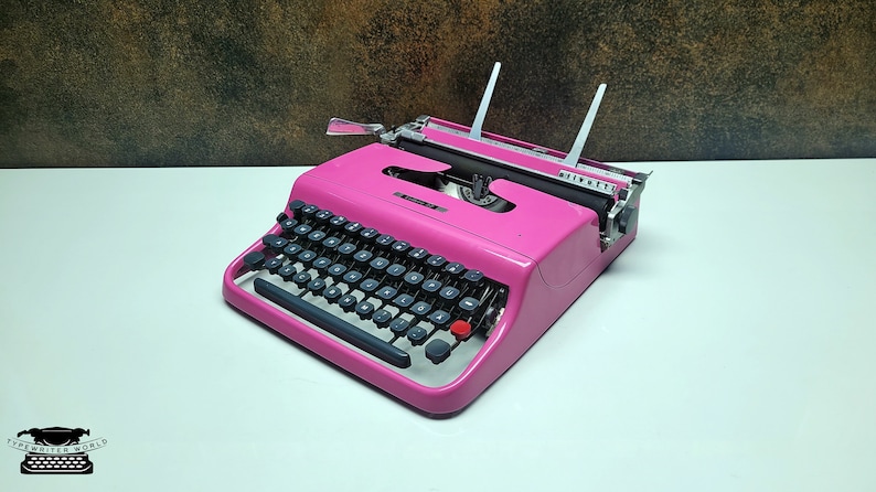 May include: A pink vintage Olivetti Lettera 32 typewriter with a black keyboard and a red return key.