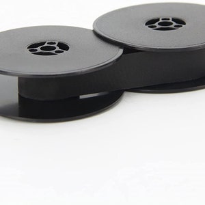 May include: Two black plastic spools for typewriter ribbon, connected by a black ribbon.