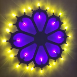 May include: A flower-shaped light fixture with a dark frame and purple petals. Each petal has a small, bright pink light in the center. The fixture is surrounded by small, yellow lights, creating a glowing effect.