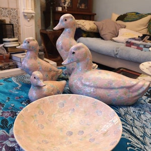 May include: A set of four pink and blue ceramic duck figurines with floral patterns, displayed on a pink and blue floral patterned bowl.