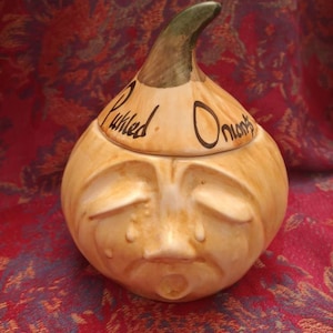 May include: A ceramic onion-shaped jar with a green top and a crying face. The jar is labelled "Pickled Onions".