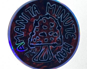 Könnte beinhalten: Ein runder Aufkleber mit einem holografischen, rot-schwarzen, strukturierten Hintergrund. In der Mitte befindet sich eine schwarze Strichzeichnung eines Pilzes mit Punkten. Der Text AMANITA MINUTE MAN steht in einem Bogen um den Pilz, TKC darunter.