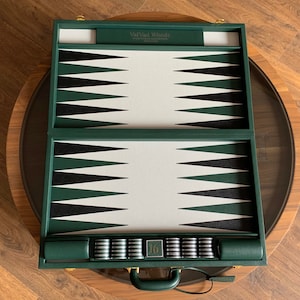 May include: A green leather backgammon set with a white and black playing surface. The set includes 15 checkers and a carrying case with a handle.