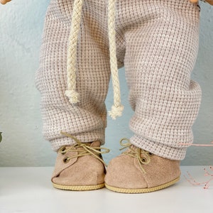Könnte beinhalten: Ein Paar hellbraune Baby-Schuhe aus Wildleder mit Schnürsenkeln. Die Schuhe haben eine hellbraune Sohle und sind mit einem hellbraunen Schnürsenkel gebunden.