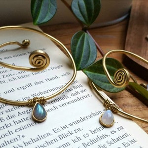 Könnte beinhalten: Zwei goldfarbene Armbänder mit einem Spiraldesign und einem tropfenförmigen Stein. Die Steine sind hellblau und weiß.