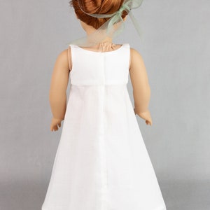 May include: A white doll dress with a lace trim and a green ribbon in the doll's hair.