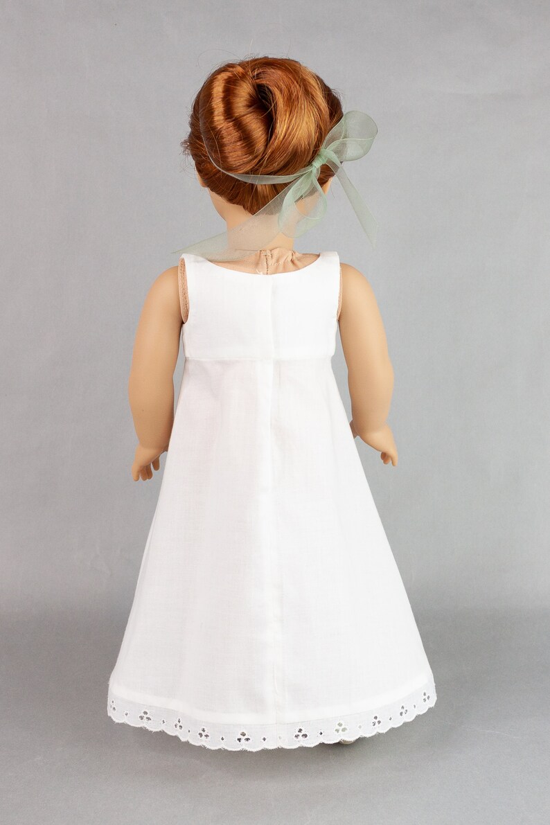 May include: A white doll dress with a lace trim and a green ribbon in the doll's hair.