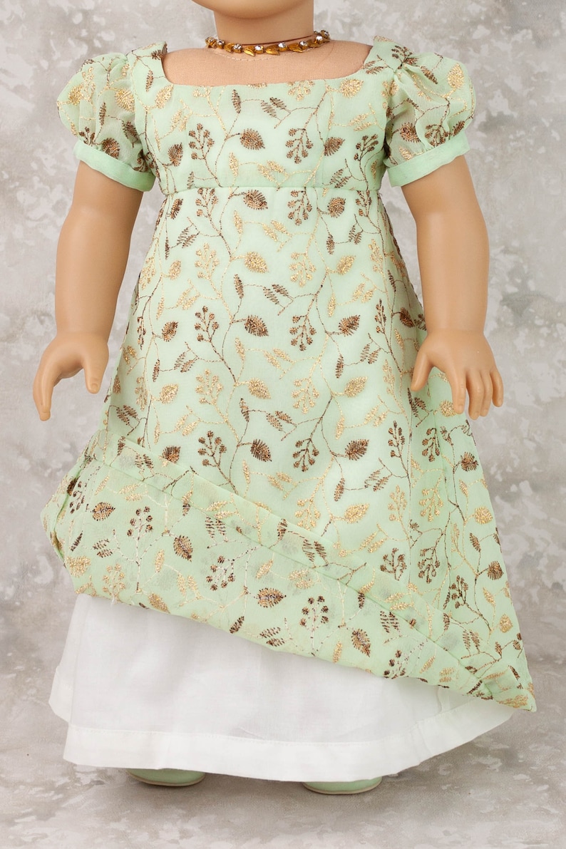 May include: A mint green doll dress with gold embroidered floral patterns. The dress features short sleeves, a square neckline, and a white underskirt. A gold-toned necklace is visible.