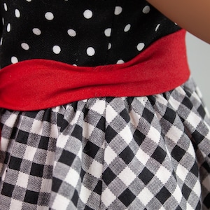May include: A black and white gingham dress with a red ribbon around the waist. The top of the dress is black with white polka dots.