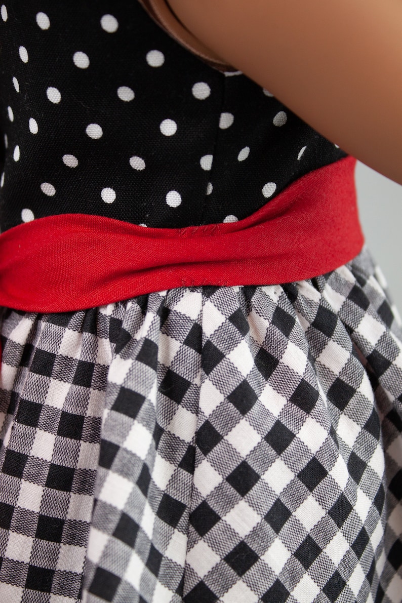 May include: A black and white gingham dress with a red ribbon around the waist. The top of the dress is black with white polka dots.