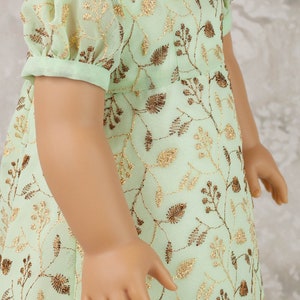 May include: A mint green doll dress with gold floral embroidery. The dress features short, puffed sleeves and a square neckline. A gold-toned necklace with clear accents is also visible.