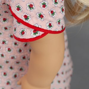 May include: A pink dress with a red trim and a floral pattern. The dress has a short sleeve and a fitted bodice.