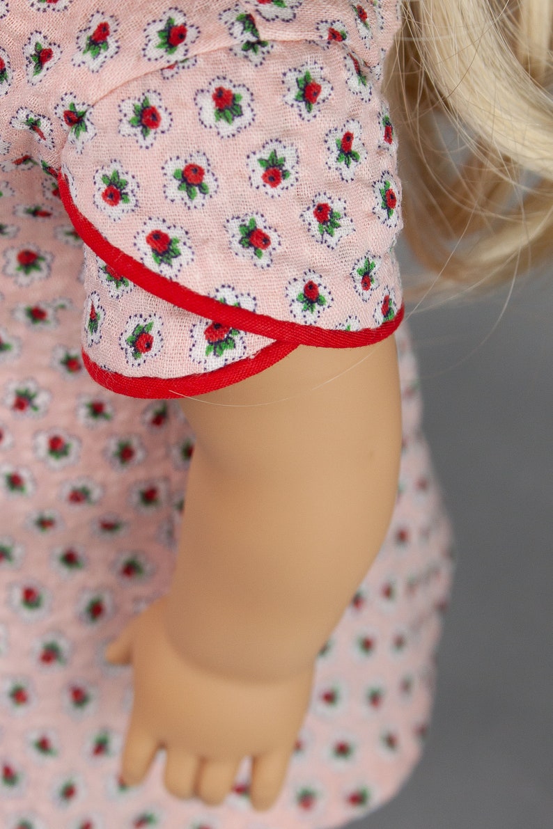 May include: A pink dress with a red trim and a floral pattern. The dress has a short sleeve and a fitted bodice.