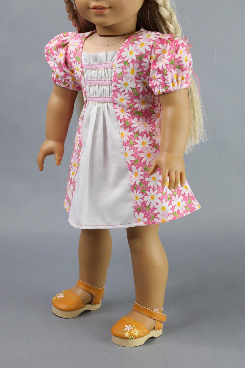 This 18 inch doll Shirred Front Dress PDF Sewing pattern is styled from the 1970s. This dress has a center front panel with shirring in the bodice extends to the skirt. There are two options for shirring in the center front panel. You may sew gathers and then apply a ⅛ to ¼ inch ribbon or gather the front section with elastic for a smocked effect. There are two sleeve options for the dress: a puff sleeve option or sleeveless. The neckline on dress is square and the skirt is semi-full.