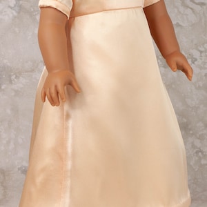 May include: A peach-colored satin doll dress with short, puffed sleeves and a square neckline. The dress features a fitted bodice and a flowing skirt. A pearl necklace with a pendant is visible.