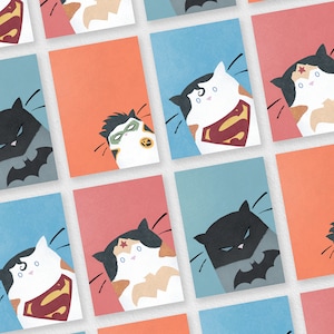 May include: A set of nine illustrated cards featuring cats dressed as superheroes. The cards are in a grid pattern with a light blue, orange, or pink background. The cats are dressed as Superman, Wonder Woman, Batman, and Robin.