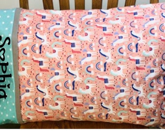 May include: A pink pillow with a white unicorn and rainbow pattern. The pillow has a teal and white polka dot fabric on the side with the name "Sophia" embroidered in black.