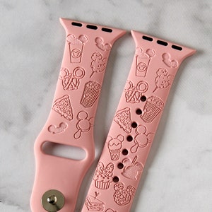 May include: Two pink silicone Apple Watch bands with a Disney Parks food and drink pattern. The bands feature embossed images of Mickey Mouse, Minnie Mouse, popcorn, ice cream, and other treats.