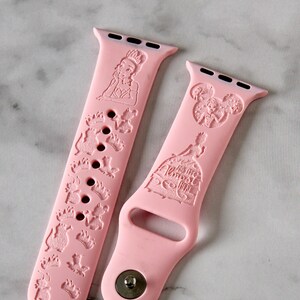 May include: Two pink Apple Watch bands with Disney character designs. One band features a princess with a crown and the other features a castle with the text "Happily Ever After".