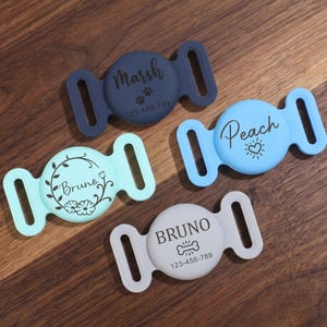 May include: Four silicone pet collar tags in dark blue, light blue, mint green, and light gray. Each tag features a central circular area with custom text and graphics, including names like Marsh, Peach, and Bruno, plus phone numbers and icons.