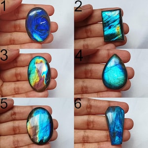 May include: Six polished labradorite gemstones are displayed, each with unique shapes and sizes. The stones exhibit shimmering colours of blue, green, and gold. The gemstones are held in a hand, highlighting their natural beauty and colour variations.