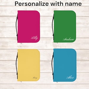 Könnte beinhalten: Vier personalisierte Reißverschlussetuis in Pink, Grün, Gelb und Blau. Jedes Etui hat einen schwarzen Griff und einen Namen in weißer Schrift: Lilly, Andrew, Mary und Alex. Der Text "Mit Namen personalisieren" steht oben.