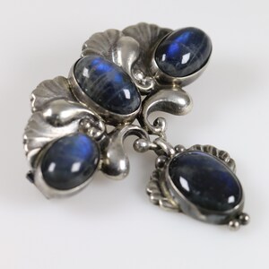 Puede incluir: Un broche de plata con cuatro cabujones de piedra lunar azul engastados en un dise&ntilde;o floral.