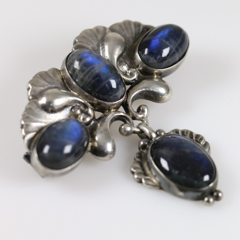 Puede incluir: Un broche de plata con cuatro cabujones de piedra lunar azul engastados en un dise&ntilde;o floral.