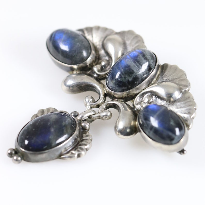 Puede incluir: Un broche de plata con cuatro piedras azules ovaladas engastadas en un dise&ntilde;o floral decorativo.