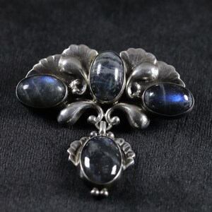Puede incluir: Un broche de plata con un dise&ntilde;o floral y tres piedras ovaladas azules.