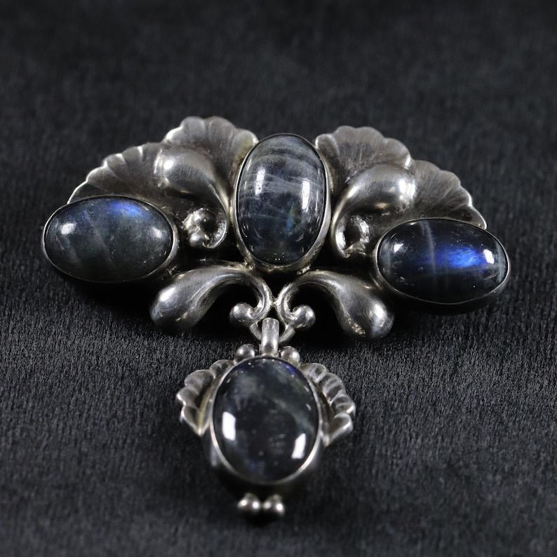 Puede incluir: Un broche de plata con un dise&ntilde;o floral y tres piedras ovaladas azules.